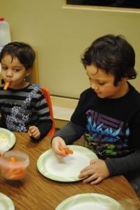 Two children sitting at a table eating food.