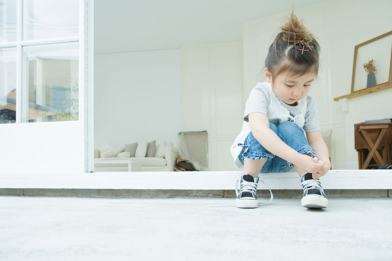 A little girl sitting on the ground tying her shoes.