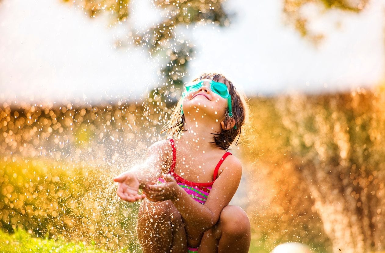 A little girl playing with water in the yard.